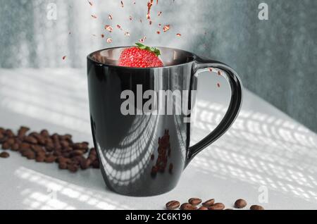 Kaffee in einem Becher und Erdbeeren mit einem Spritzer. Vor dem Hintergrund durchbrochener Schatten aus dem Fenster und verstreuter Kaffeebohnen Stockfoto