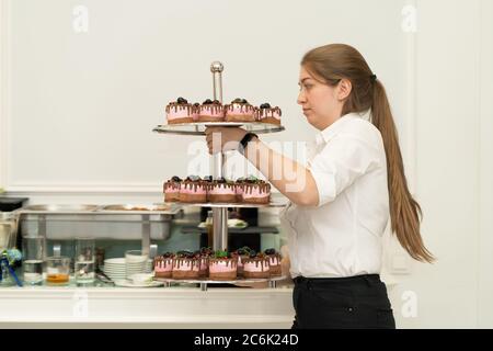 Mädchen der Kellner macht ein dreistufiges Tablett mit Kuchen. Stockfoto