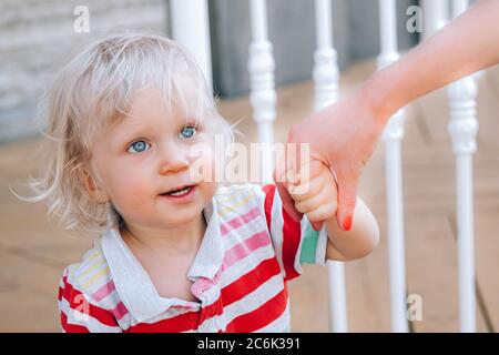 Niedlicher kleiner blonder Junge mit blauen Augen, die die Hand seiner Mutter halten und versuchen, draußen zu gehen. Erste Schritte, Elternschaft, Mutter-Sohn-Konzept. Stockfoto