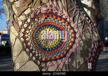 Spektakuläre handgemachte bunte Strickverzierung auf einem Baumstamm. Stockfoto