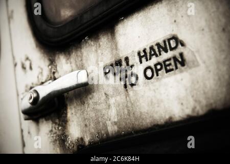Schild „zum Öffnen den Griff ziehen“ neben dem Griff der schmutzigen weißen Tür. Stockfoto