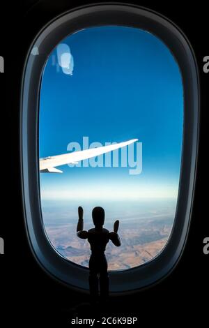 Ein hölzernes menschliches Manikin, das durch ein Flugzeugfenster auf die Landschaft unten schaut Stockfoto