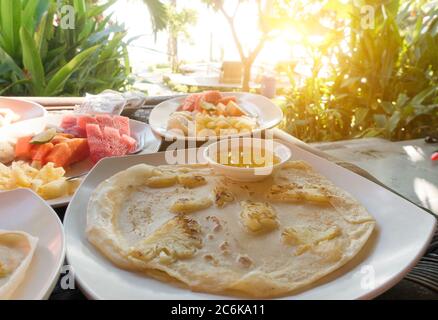 Frühstück, Pfannkuchen und Obst, wird auf der Außenterrasse mit Blick auf die und tropischen Pflanzen serviert. Indonesien Stockfoto