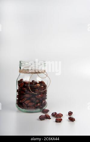 Offenes Glas mit verbrannten Mandeln. Weißer Hintergrund mit Kopierbereich im oberen Teil des Bildes. Einige Mandeln verteilt sich herum. Glasierte Mandeln im Glas mit Stockfoto