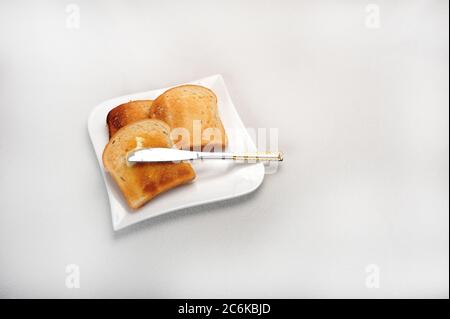 Drei Scheiben Toast auf weißem Teller. Weiße Oberfläche. Messer mit Butter. Stockfoto