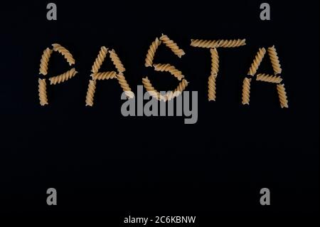 Das Wort Pasta mit Pastaschrauben geschrieben. Platz im unteren Teil des horizontalen Bildes kopieren. Schwarzer Hintergrund. Stockfoto