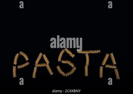 Das Wort Pasta mit Pastaschrauben geschrieben. Kopieren Sie den Platz im oberen Teil des horizontalen Bilds. Schwarzer Hintergrund. Stockfoto