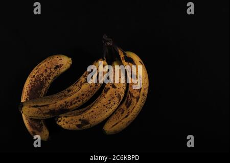 Vier überreife Bananen auf schwarzer Oberfläche. Hochwinkelaufnahme mit Kopierbereich im oberen und rechten Teil des Fotos. Low-Key-Foto. Stockfoto