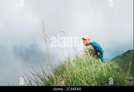 Happy Backpacker Mann hat eine Pause genießen bewölkt Talboden Wandern durch die neblig bewölkten Wetter Bergkette. Aktive Sport Rucksack hea Stockfoto