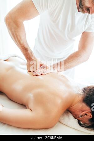 Bärtiger Masseur, der während der Massage des weiblichen Körpers auf der Scapula-Zone massiert. Ausgereifte Inhalte. Stockfoto