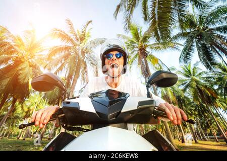 Mann in sicheren Helm Reiten ein Motorrad unter Palmen Weitwinkel-Objektiv aufgenommen Stockfoto