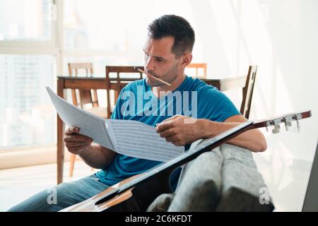 Mid Adult Man Reading Akustische Gitarre Noten In Wohnung Stockfoto