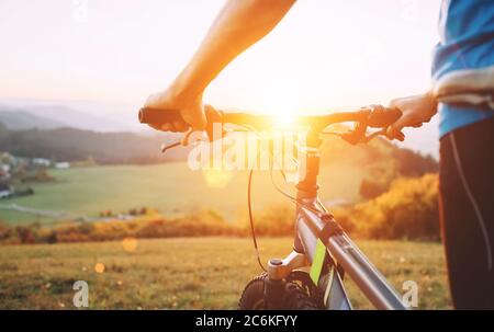 Man Hände auf dem Fahrrad Lenkrad Nahaufnahme Bild. Mann mit Fahrrad auf der Spitze des Hügels bleiben und den Sonnenuntergang genießen. Stockfoto