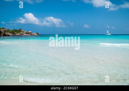 Meereswellen, weißes Boot, makellose blaue Lagune und Granitfelsen am Strand von Anse Coco, La Digue Island, Seychellen Stockfoto