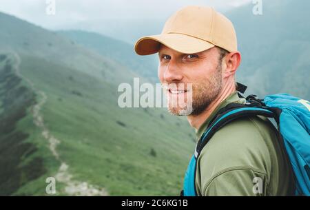Portrait des Backpacker-Mannes in Baseballmütze, der durch den neblig bewölkten Bergwanderweg mit Rucksack geht. Aktiv Sport Backpacking gesund li Stockfoto