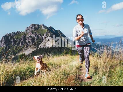 Fröhlich lächelnde Hündin beim Joggen am Wanderweg mit ihrem Beagle-Hund. Canicross Laufen gesunde Lebensweise Konzept Bild. Stockfoto