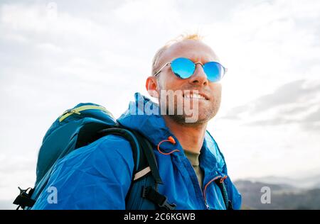 Backpacker Mann Lifestyle Portrait genießen Berglandschaft. Er trägt in blauem Regenmantel Poncho und blaue Sonnenbrille. Aktiv Sport Rucksackreisen Gesundheit Stockfoto