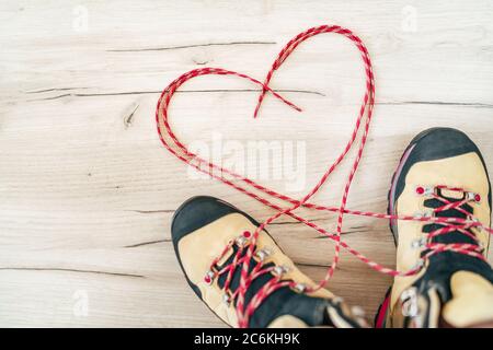 Konzeptionelles Bild des Paares neue Trekkingstiefel auf dem Holzboden Hintergrund mit freigelassenen langen Schnürsenkeln hinter in Herzform liegend. Stockfoto