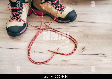 Konzeptionelles Bild des Paares neue Trekkingstiefel auf dem Holzboden Hintergrund mit freigelassenen langen Schnürsenkeln hinter in Herzform liegend. Stockfoto