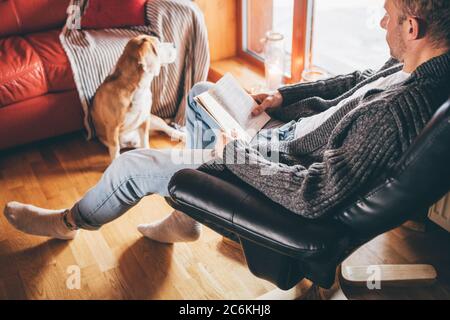 Mann liest Buch auf der gemütlichen Couch zu seinem Beagle Hund in gemütlicher Wohnatmosphäre. Friedliche Momente des gemütlichen Hauses Konzept Bild. Stockfoto