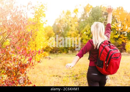 Junge Frau mit Rucksack hebt die Hände und genießen Sie die Aussicht im Herbst Park Stockfoto