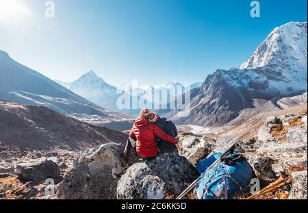 Umarmende Paare auf der Everest Base Camp Trekkingroute bei Dughla 4620m. Backpacker links Rucksäcke und Trekking Stöcke und genießen Talblick wit Stockfoto