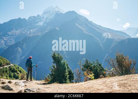 Junger Wanderer Backpacker Mann mit Trekking Stöcke genießen die Thamserku 6608m Berg mit fliegenden Rettungshubschrauber in der Höhe Acclimatizati Stockfoto