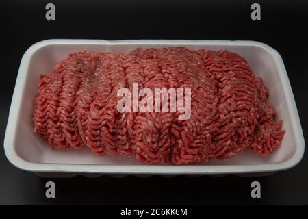 Rohes Hackfleisch (gemahlen) in einem weißen Styroporbehälter, isoliert auf schwarzem Hintergrund mit Platz für Text Stockfoto