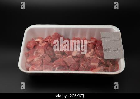 Rohes gewürfeltes Fleisch (in Würfel geschnitten) in einem weißen Styropor-Behälter mit Barcode darauf isoliert auf schwarzem Hintergrund Copy Space für Text Stockfoto