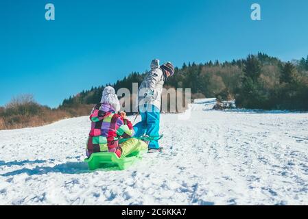 Kleiner Junge trägt Mädchen im Schlitten und genießen Winter Rodeln Zeit. Lustige Winterferien Ausgaben Konzept Bild. Stockfoto