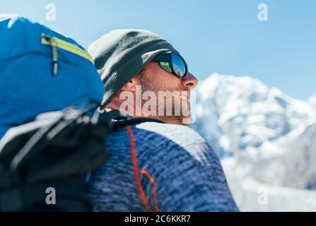 Portrait von unrasierte Wanderer Mann mit Rucksack und UV-Schutz Sonnenbrille auf Taboche 6495m peakk Hintergrund, Er genießt die Aussicht auf die Berge während Evere Stockfoto