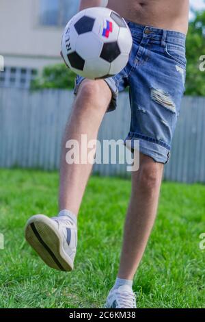 Junger Mann in Jeans und weißen Turnschuhen, der im Freien Fußball spielt. Amateur-Fußballspieler minzen den Ball Stockfoto