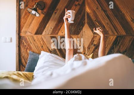 Faule Frau, die unter der weißen Decke auf dem Leinenbett lag und die frische Kaffeetasse am frühen Morgen hielt. Fauler Tag und "Kaffee im Bett" con Stockfoto