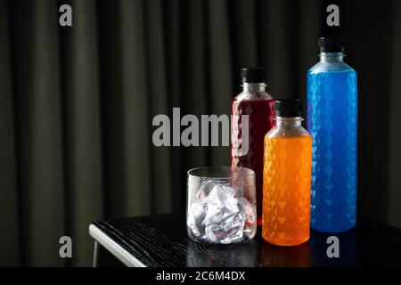 PET-Plastikflasche in verschiedenen Größen, Nektar in verschiedenen Farben und Eis in ein Glas, kristallklare Flasche auf schwarzem Hintergrund Alle leuchtet gut Stockfoto