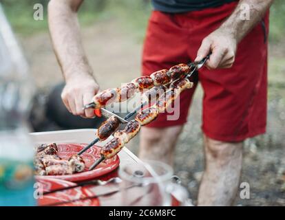 Mann Kochen Fleisch Würste Grill in der Natur auf dem Campingplatz. Lokaler Tourismus Wochenend-Ferien Stockfoto