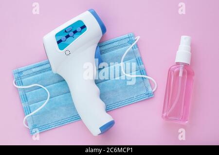 Berührungsloses Infrarot-Digitalthermometer, Handdesinfektionsmittel und medizinische Maske auf rosa Hintergrund. Ein Werkzeug zur Messung der menschlichen Temperatur. Covid-19 vorh Stockfoto