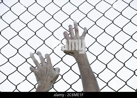 Gebleicht gefiltertes Bild von Händen in verzweifeltem Griff auf Netz verdrahteten Zaun, symbolisiert Gefangenschaft, hoffnungslos, Entführung, Kampf und gestresste Person. Stockfoto