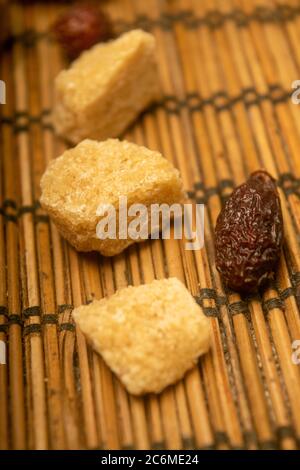 Stücke von braunem Rohrzucker und getrockneten Hagebutten auf einem Schilfmatter verstreut. Nahaufnahme Stockfoto