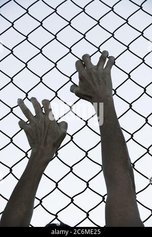 Gebleicht gefiltertes Bild von Händen in verzweifeltem Griff auf Netz verdrahteten Zaun, symbolisiert Gefangenschaft, hoffnungslos, Entführung, Kampf und gestresste Person. Stockfoto