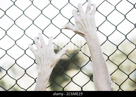 Gebleicht gefiltertes Bild von Händen in verzweifeltem Griff auf Netz verdrahteten Zaun, symbolisiert Gefangenschaft, hoffnungslos, Entführung, Kampf und gestresste Person. Stockfoto