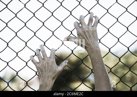 Gebleicht gefiltertes Bild von Händen in verzweifeltem Griff auf Netz verdrahteten Zaun, symbolisiert Gefangenschaft, hoffnungslos, Entführung, Kampf und gestresste Person. Stockfoto