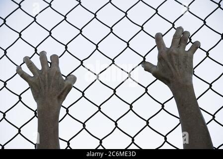 Gebleicht gefiltertes Bild von Händen in verzweifeltem Griff auf Netz verdrahteten Zaun, symbolisiert Gefangenschaft, hoffnungslos, Entführung, Kampf und gestresste Person. Stockfoto