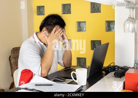 Gereifte asiatische Geschäftsmann mit beiden Händen auf Stirn in stressigen Ausdruck in der Arbeit von zu Hause Video-Telefonkonferenz in Malaysia Stockfoto