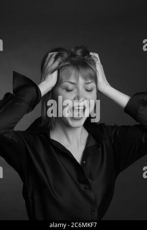 Schwarz-weiß Studioportrait einer jungen Frau mit kurzen Haaren in einer schwarzen Bluse. Sie schreit, hält ihren Kopf in den Händen. Das Konzept der Hysterie und Depression Stockfoto