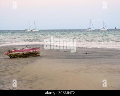 Eine kleine Holzdhow, die am Strand in Vilanculos, Mosambik, am frühen Morgen festgemacht wurde, mit vier Segelyachten im Hintergrund Stockfoto