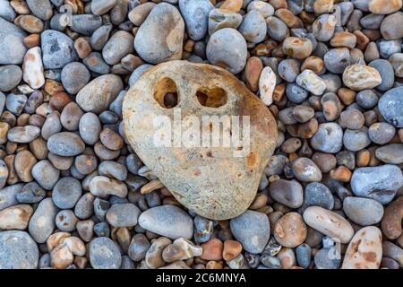 Blick auf Kieselsteine am Strand, mit einem Stein mit Löchern in der Verlegung auf Stockfoto