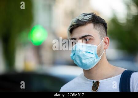 Gutaussehender junger Mann, der im Freien steht und eine medizinische Maske trägt, um andere vor der Verbreitung von Viren zu schützen Stockfoto