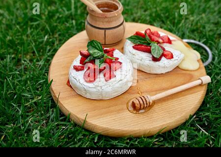 Gegrillter Camembert-Käse mit Erdbeer-, Honig- und Basilikumblättern, Delikatessen, Camembert-Käsefondue auf dem Grashintergrund. Stockfoto