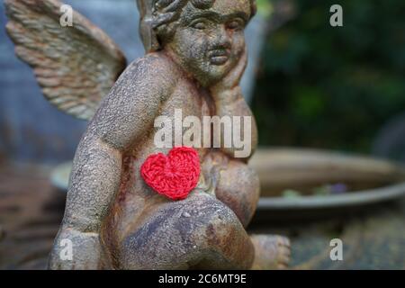 Verträumte Engelstatue mit gehäkeltem roten Herzen. Stockfoto