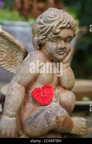 Verträumte Engelstatue mit gehäkeltem roten Herzen. Stockfoto